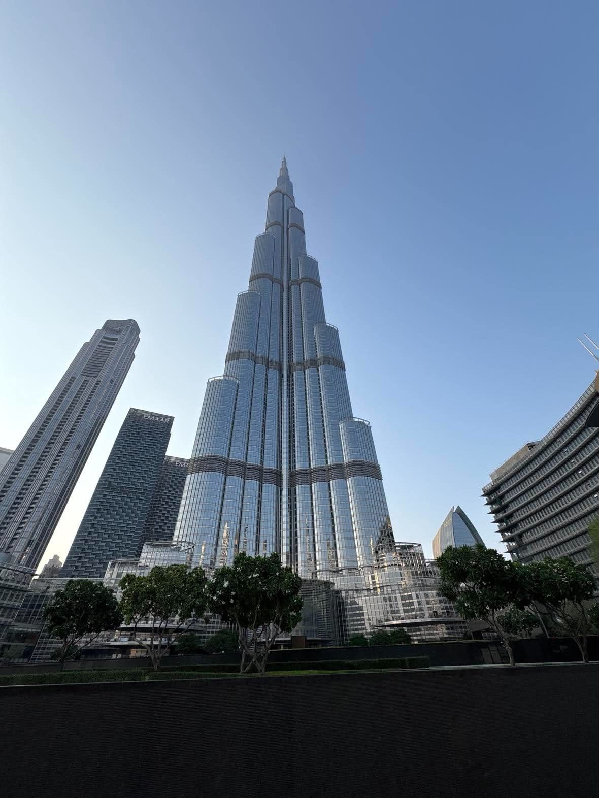Burj Khalifa seen from ground level in Downtown Dubai, neighbouring towers to the left and low sun on the glass