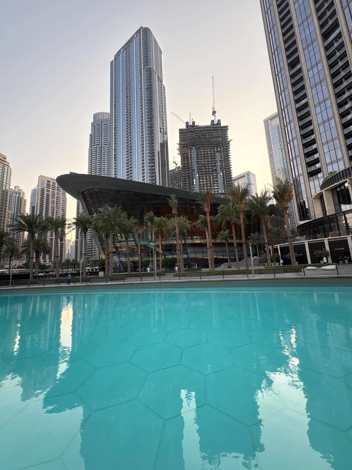 Dubai Opera's dhow-shaped building behind a row of palms, seen across the turquoise water of Burj Lake